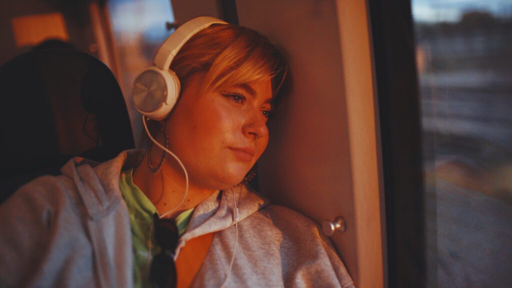 Kvinna med hörlurar som åker tåg och tittar ut genom fönstret mot morgonljuset